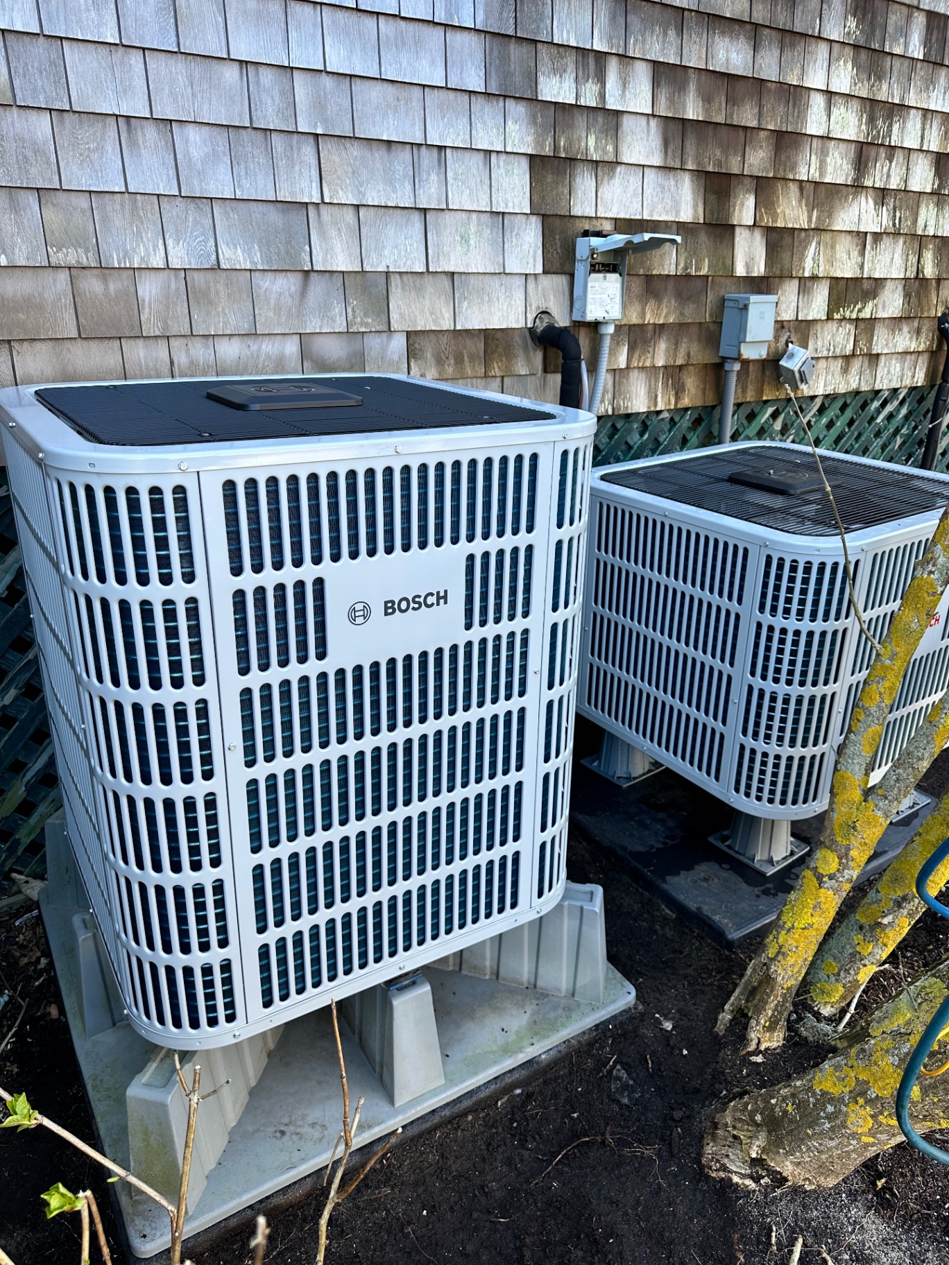 Two new Bosch heat pump condensers on pads against shingle siding